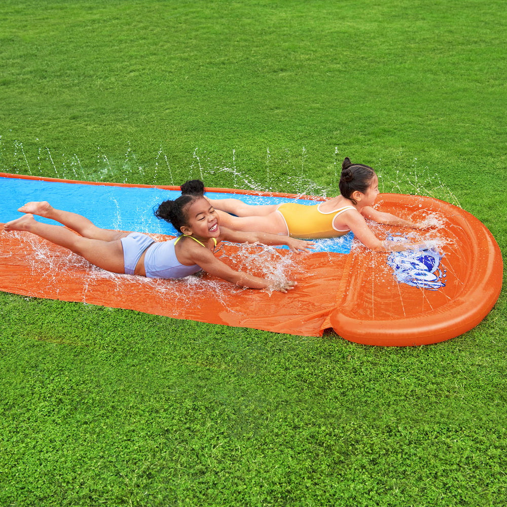 Two children sliding down an inflatable water slide on a grassy area